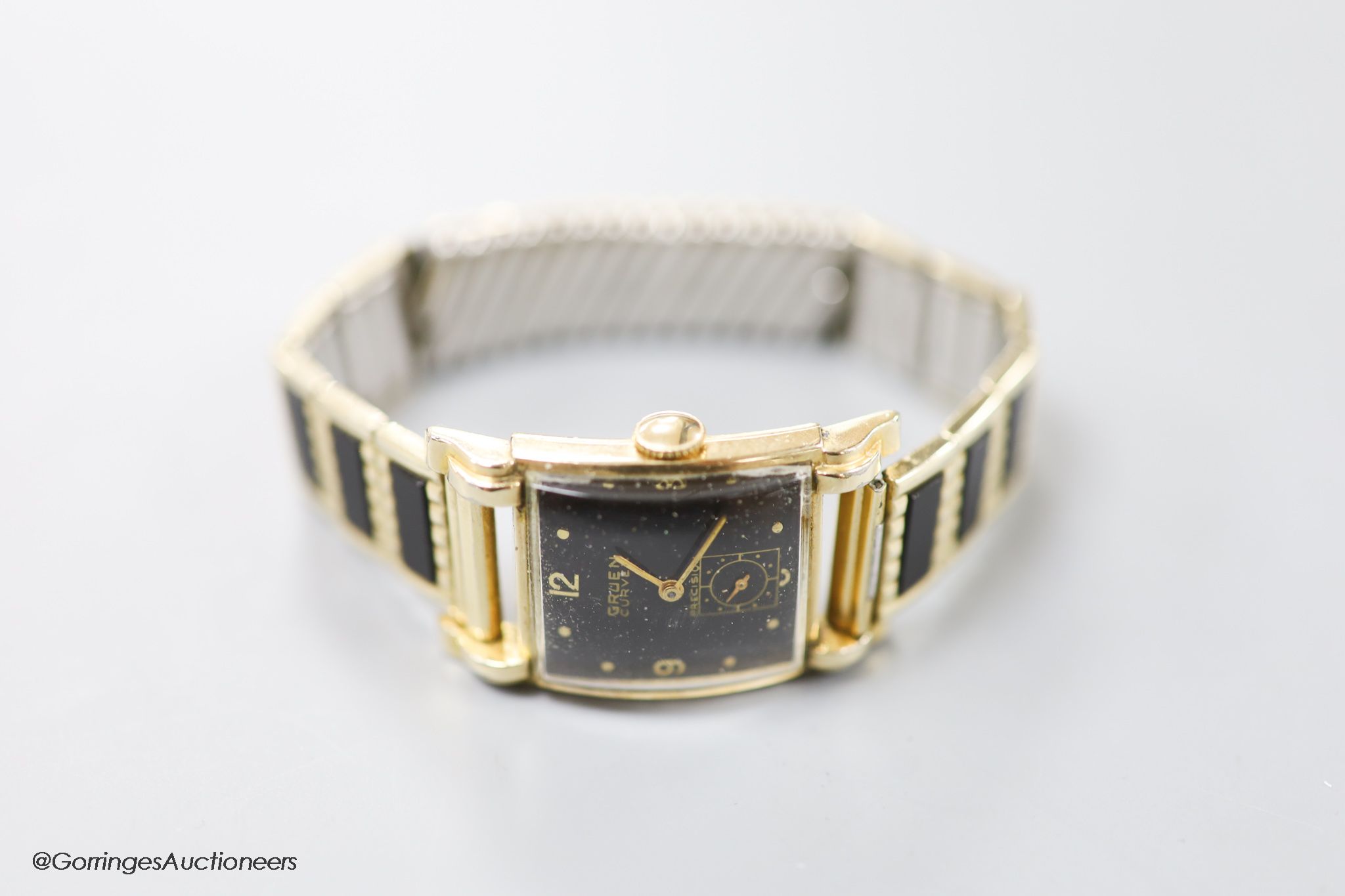 A gentleman's 1930's 10k gold filled, stainless steel Gruen Curvex Precision manual wind rectangular black dial wrist watch, on a gold plated and ceramic bracelet.